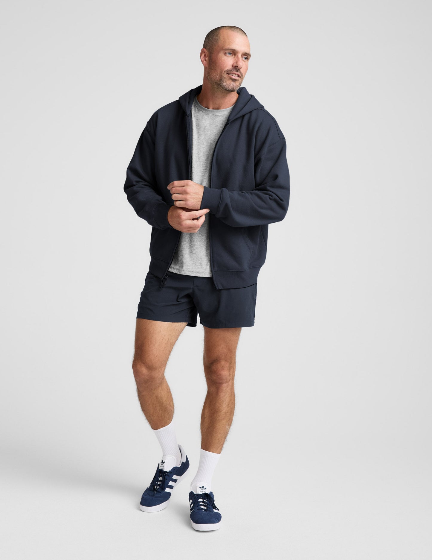 Man wearing a navy blue full zip hoodie and shorts on a plain background.
