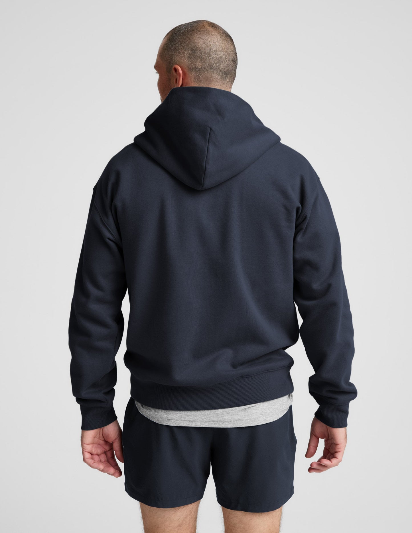 Man wearing a navy blue full zip hoodie and shorts on a plain background.