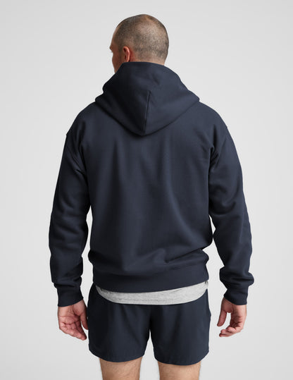 Man wearing a navy blue full zip hoodie and shorts on a plain background.