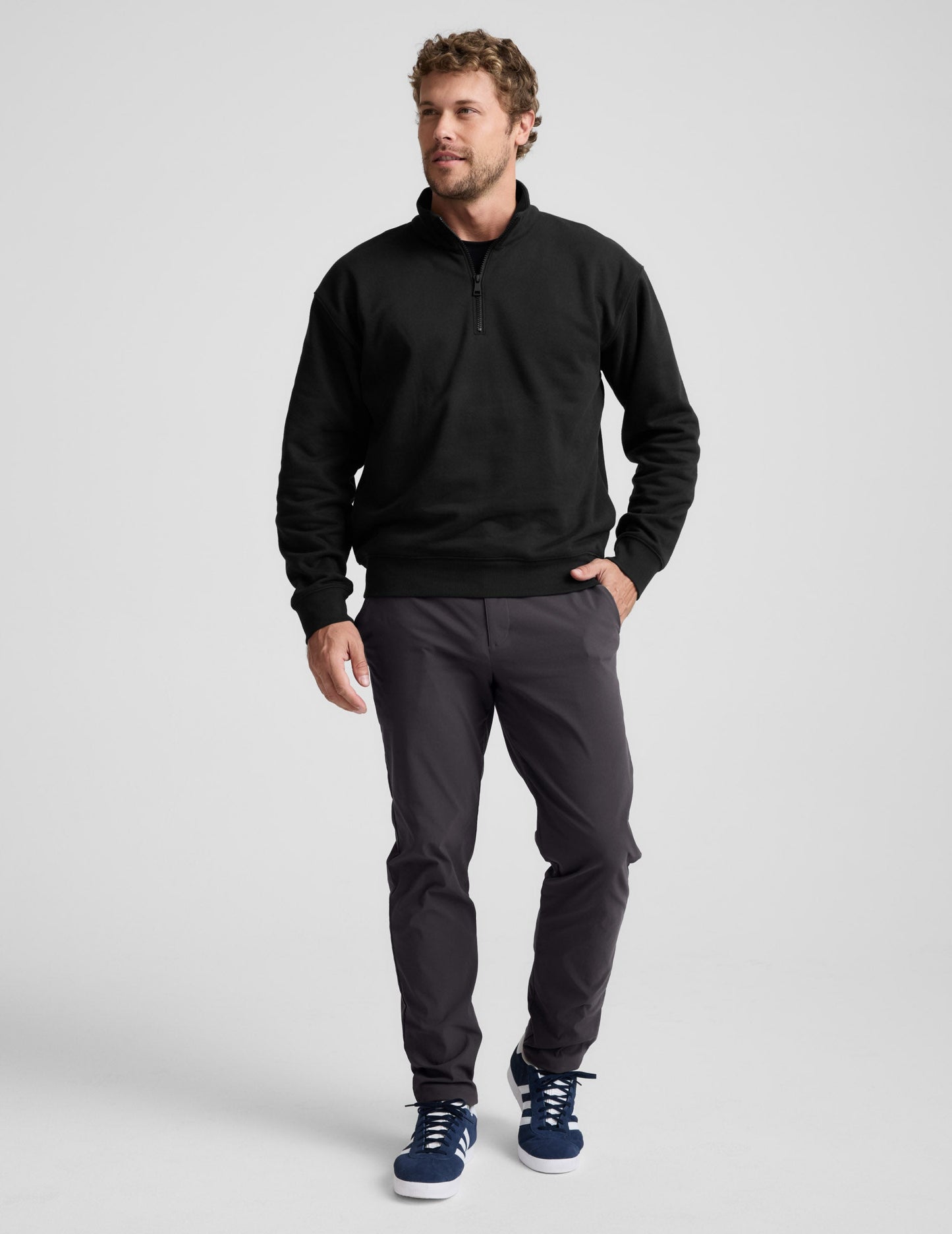 Man wearing a black quarter-zip sweatshirt and gray pants on a light gray background.