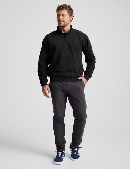 Man wearing a black quarter-zip sweatshirt and gray pants on a light gray background.