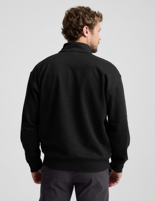Man wearing a black quarter-zip sweatshirt and gray pants on a light gray background.