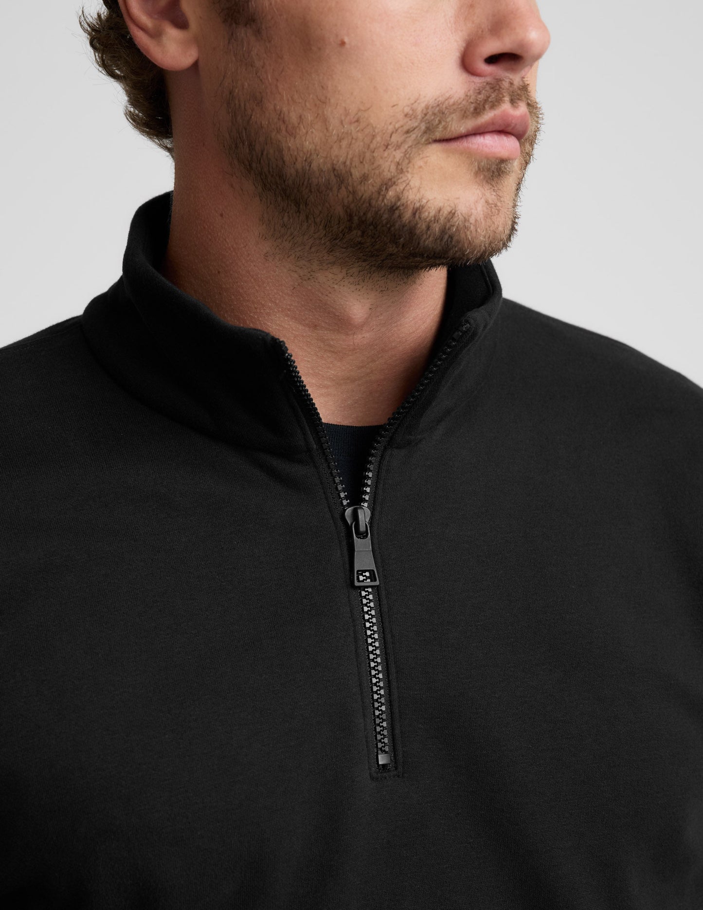 Close-up of a person wearing a black quarter-zip sweatshirt on a light gray background.