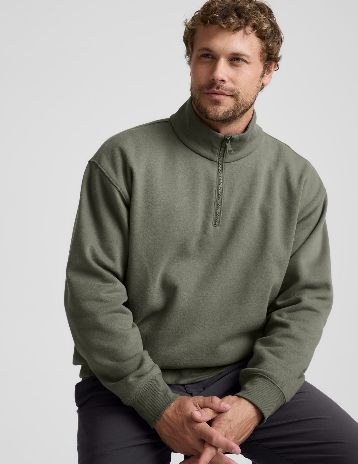 Man wearing a green quarter zip pullover and khaki pants with a plain background.