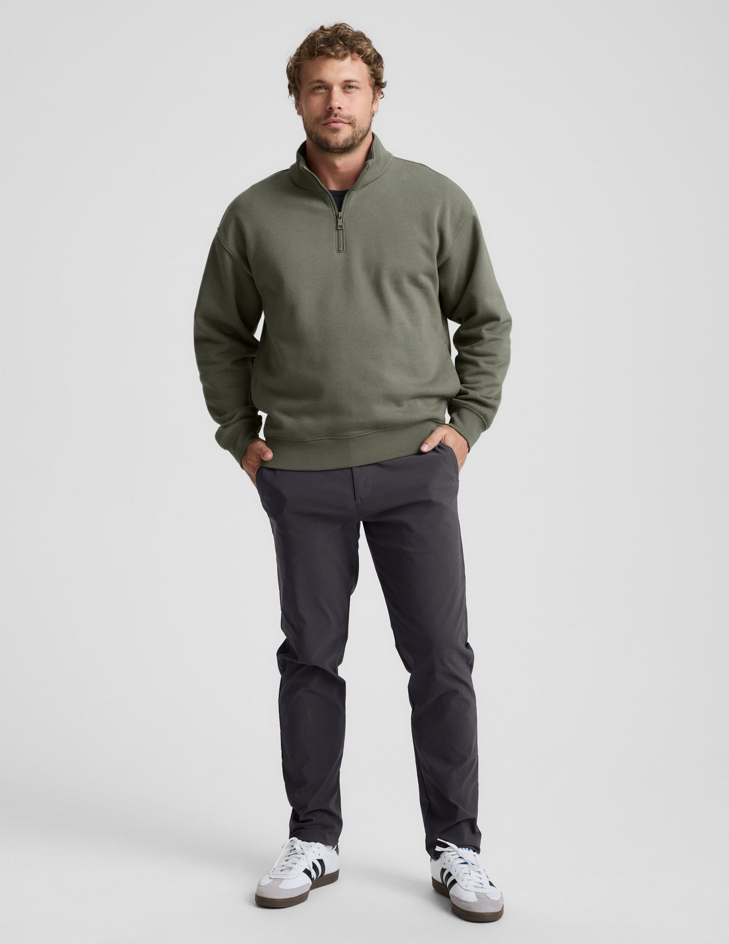 Man wearing a green quarter zip pullover and khaki pants with a plain background.