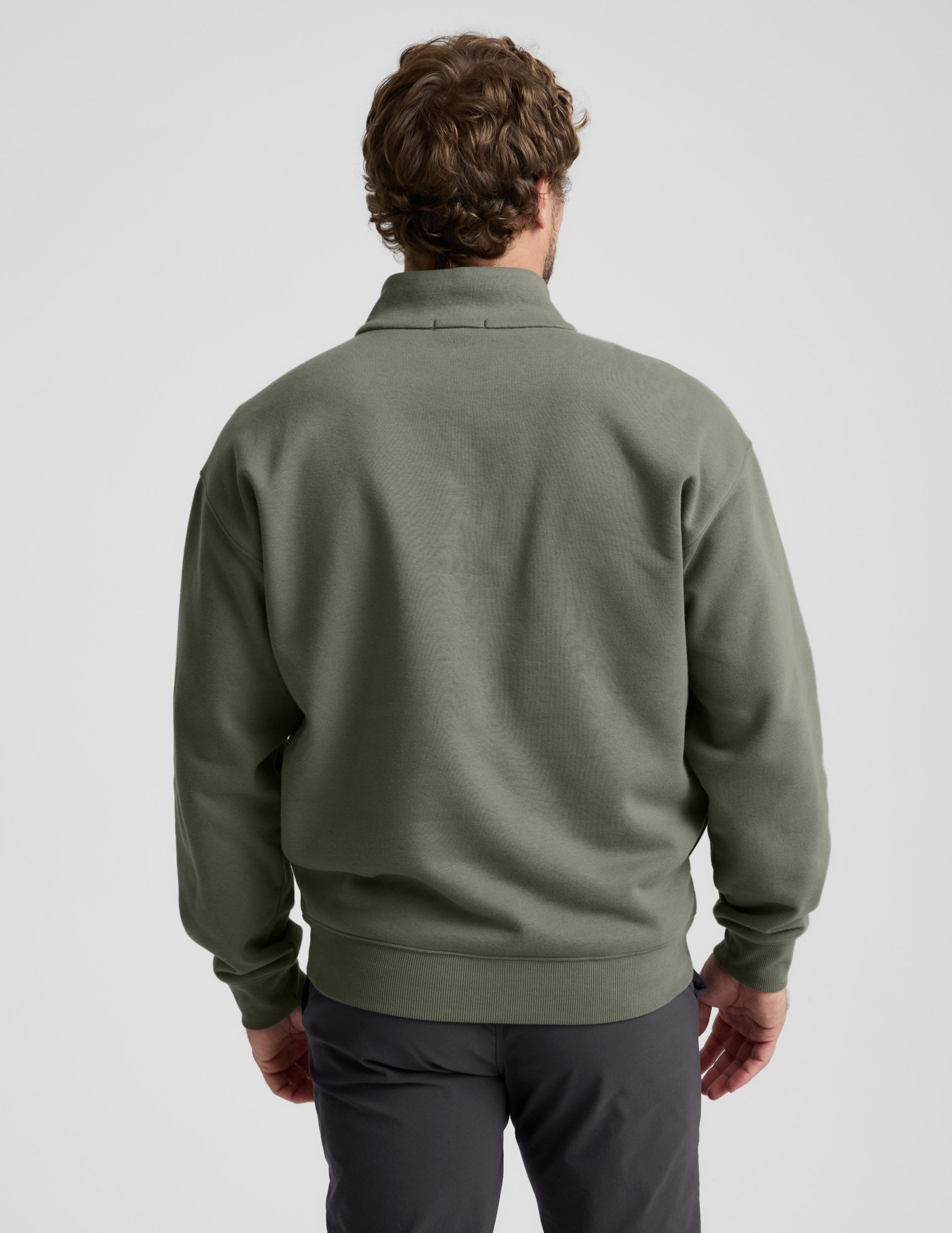 Man wearing a green quarter zip pullover and khaki pants with a plain background.