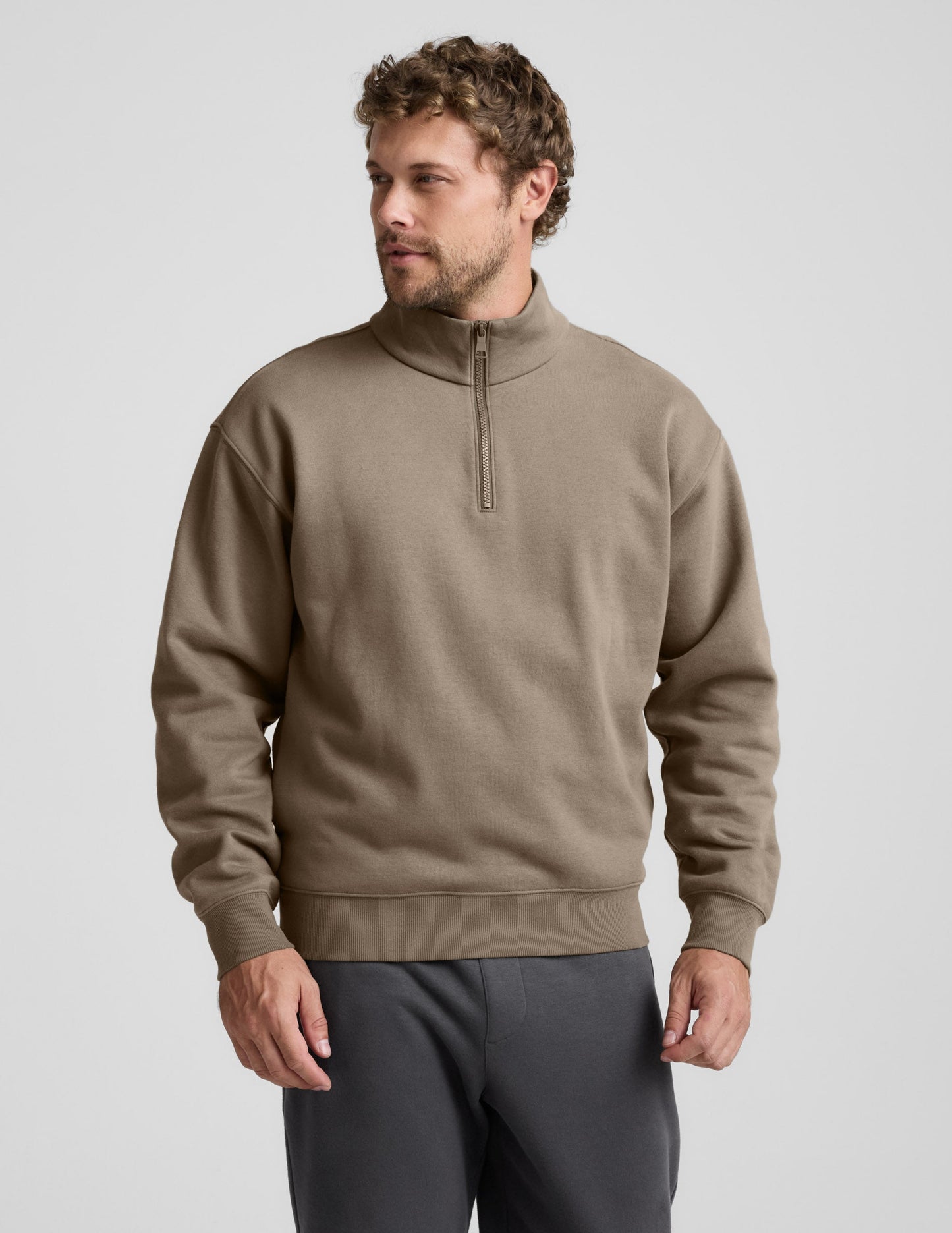 Man wearing a brown half-zip sweatshirt against a light gray background.
