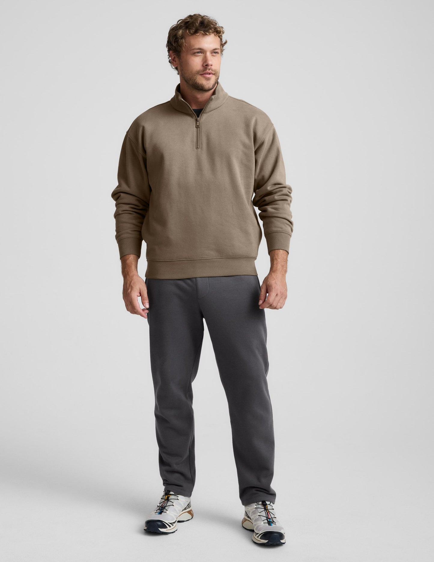 Man wearing a brown half-zip sweatshirt against a light gray background.
