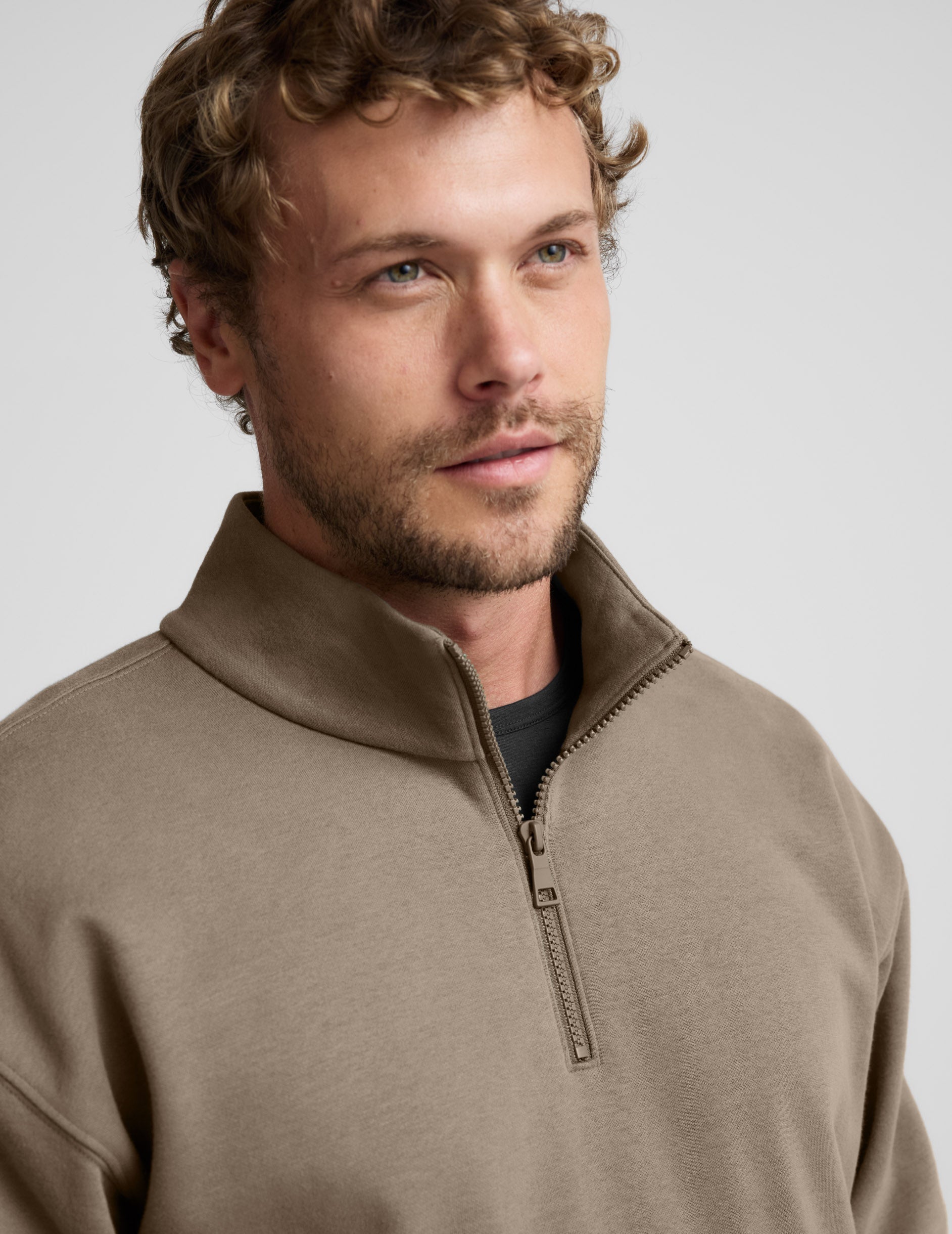 Man wearing a brown half-zip sweatshirt against a light gray background.