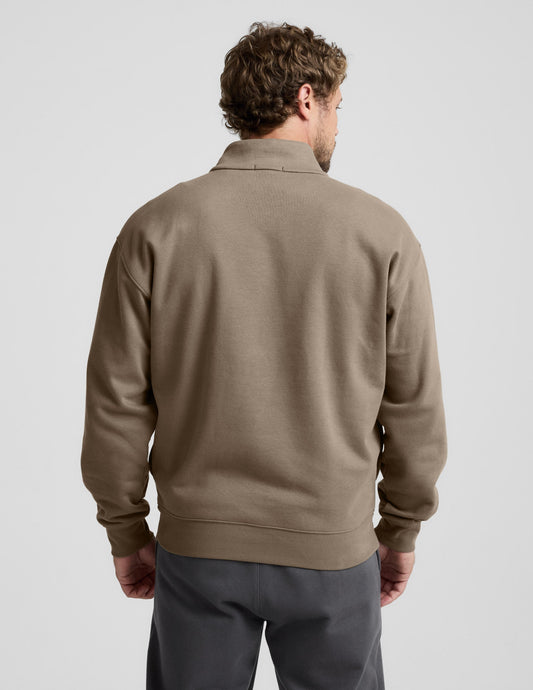 Man wearing a brown half-zip sweatshirt against a light gray background.