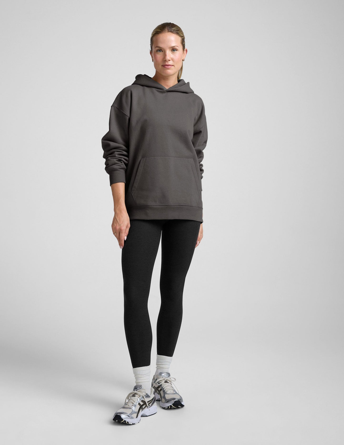 woman wearing a black hoodie with black leggings on a plain background.