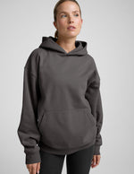 woman wearing a black hoodie with black leggings on a plain background.