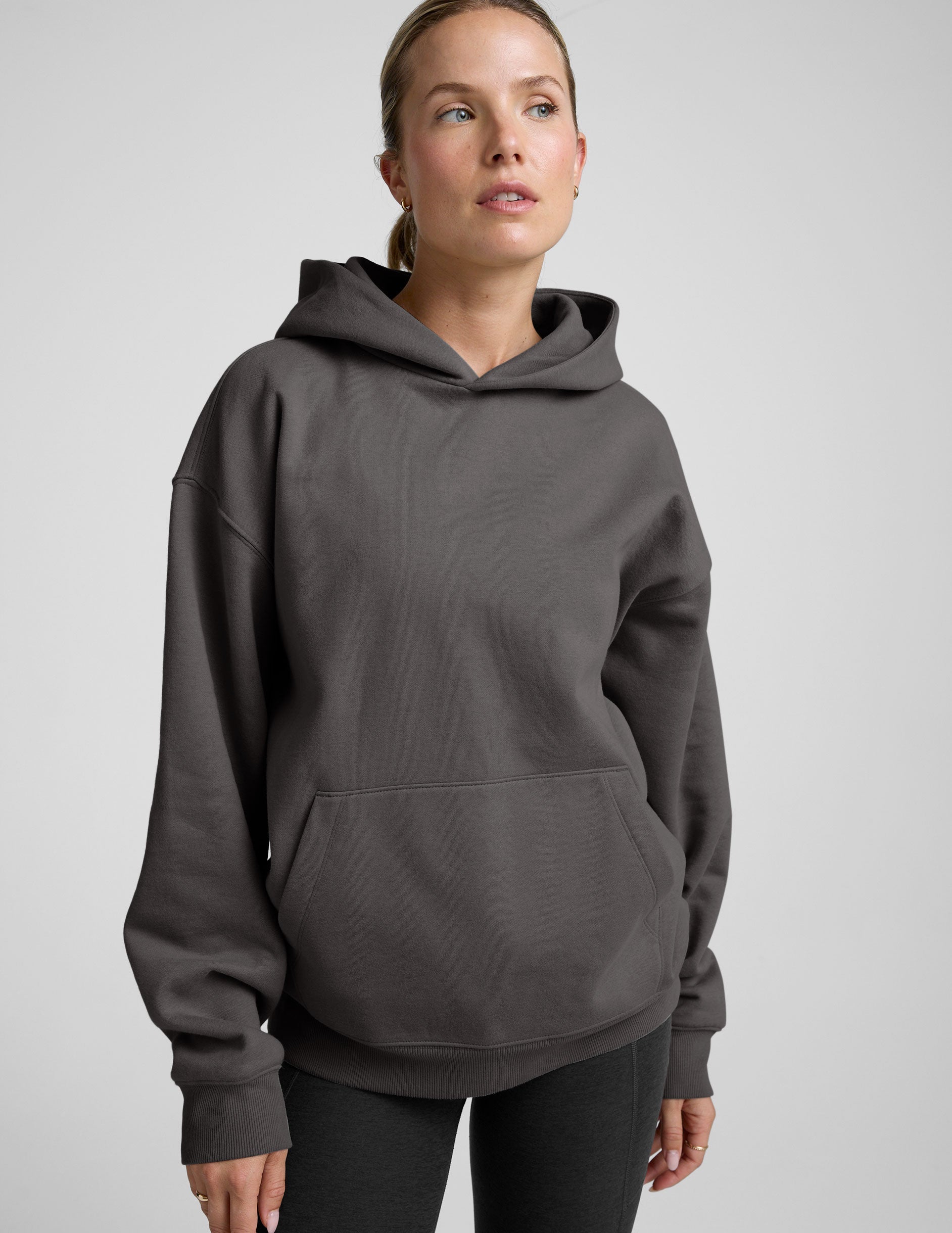 woman wearing a black hoodie with black leggings on a plain background.
