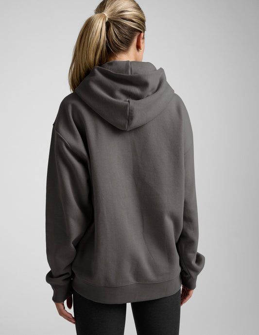 woman wearing a black hoodie with black leggings on a plain background.