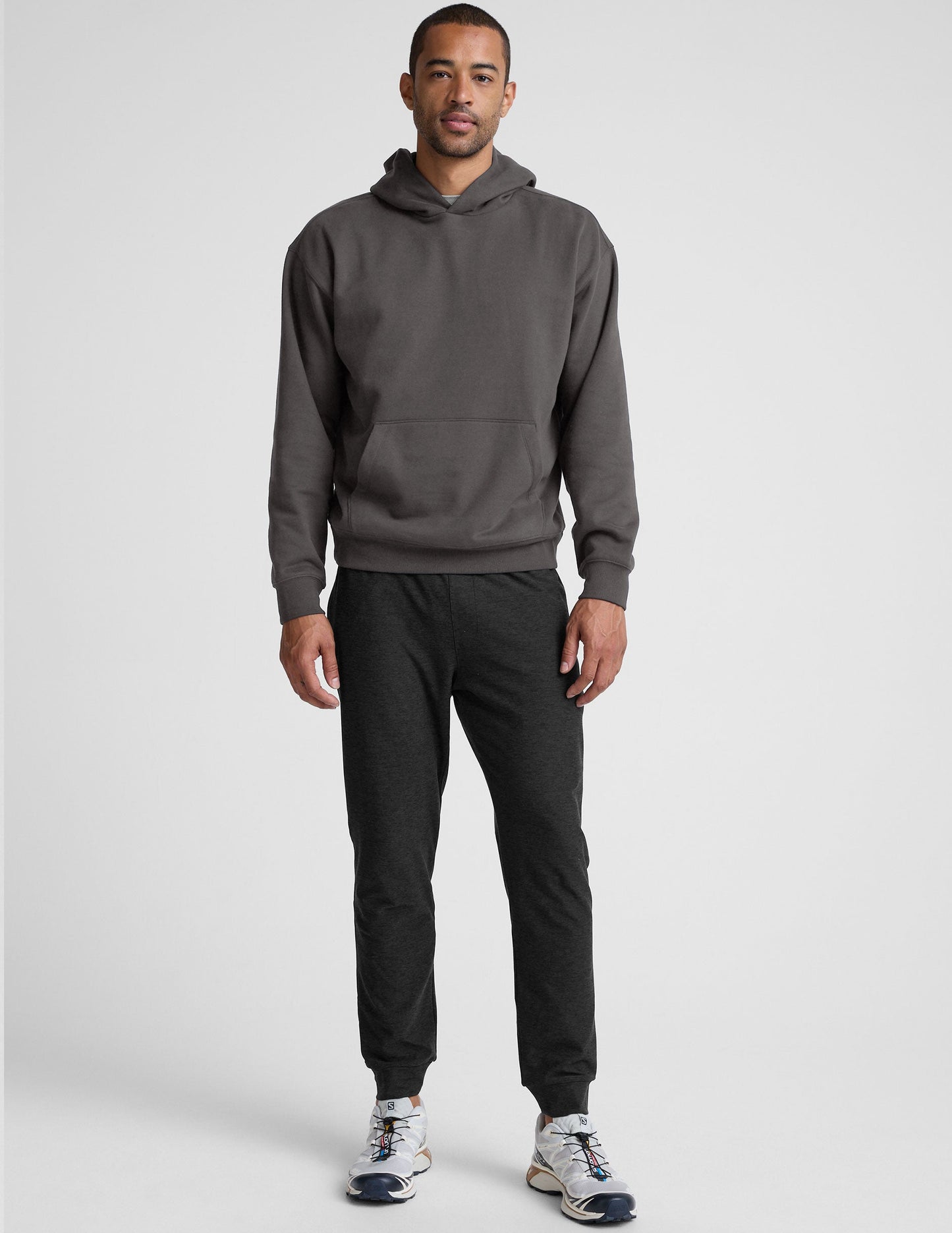 Man wearing a gray hoodie and pants on a light gray background.