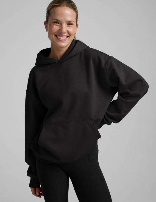 Woman wearing a black oversized hoodie and black leggings against a plain background.