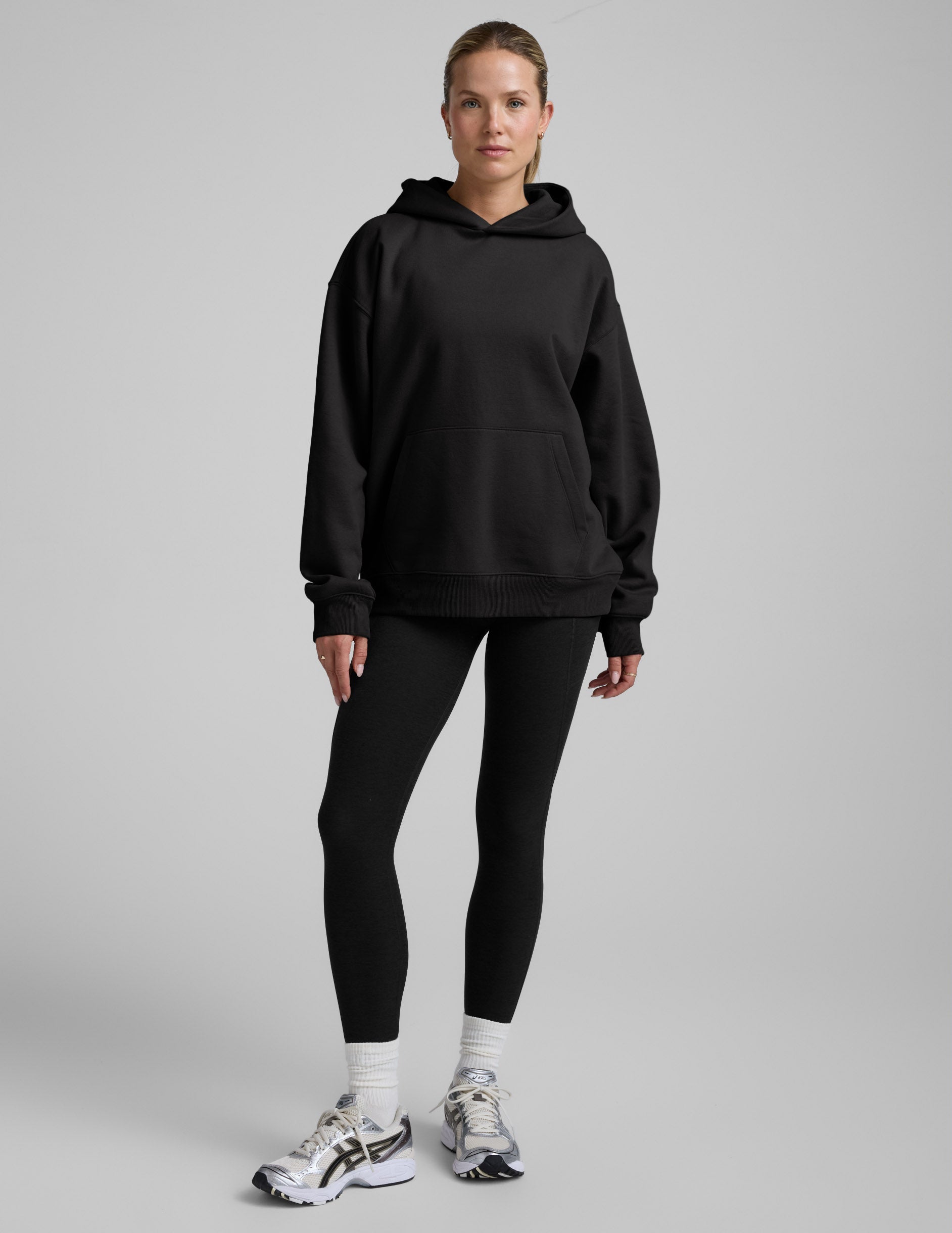 Woman wearing a black oversized hoodie and black leggings against a plain background.