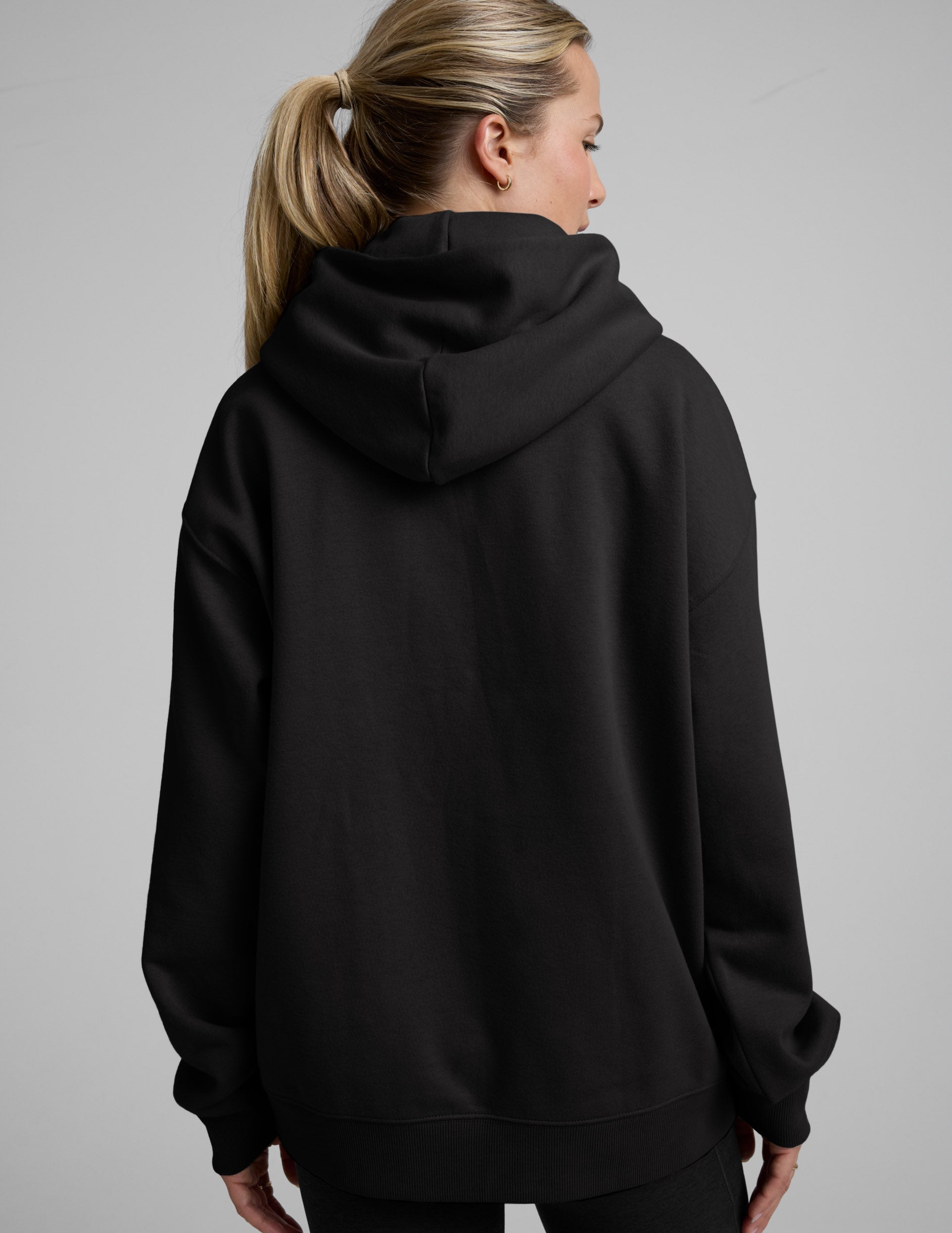 Woman wearing a black oversized hoodie and black leggings against a plain background.