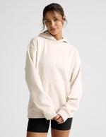 Woman wearing a white oversized hoodie and black shorts on a light gray background.