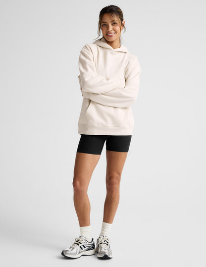 Woman wearing a white oversized hoodie and black shorts on a light gray background.