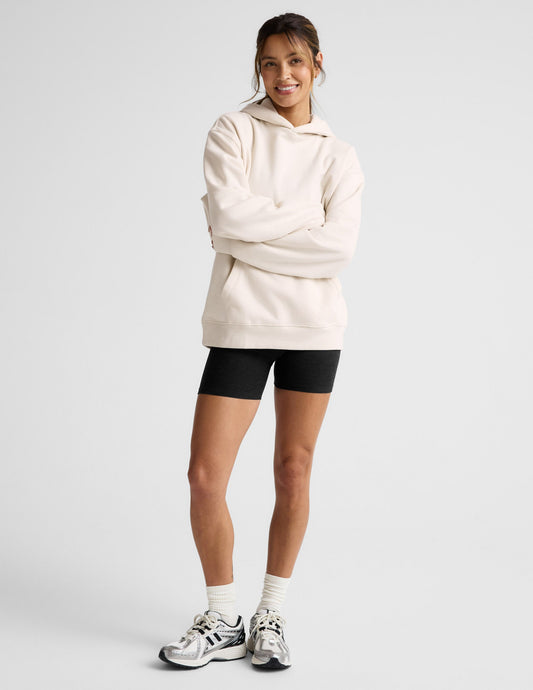 Woman wearing a white oversized hoodie and black shorts on a light gray background.