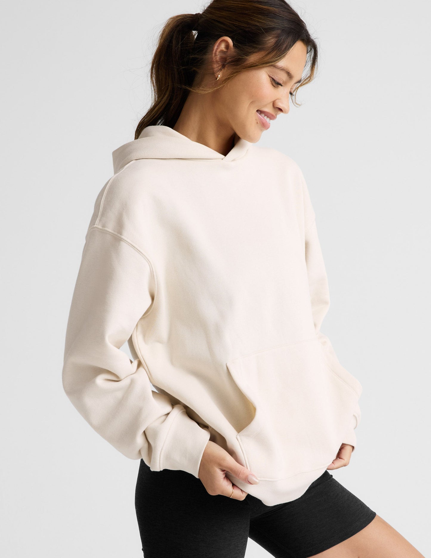 Woman wearing a white oversized hoodie and black shorts on a light gray background.