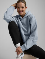 Woman wearing a light blue hoodie and black leggings on a gray background.