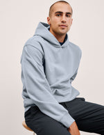 Man wearing a light blue hoodie sitting on a stool against a plain background.