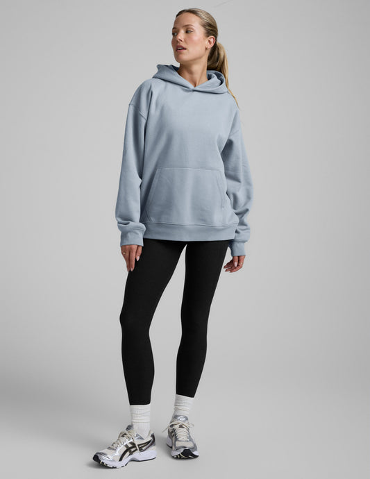 Woman wearing a light blue hoodie and black leggings on a gray background.
