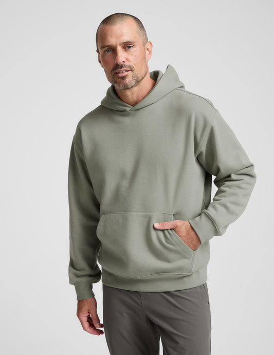 Man wearing a green hoodie and gray pants on a light gray background.