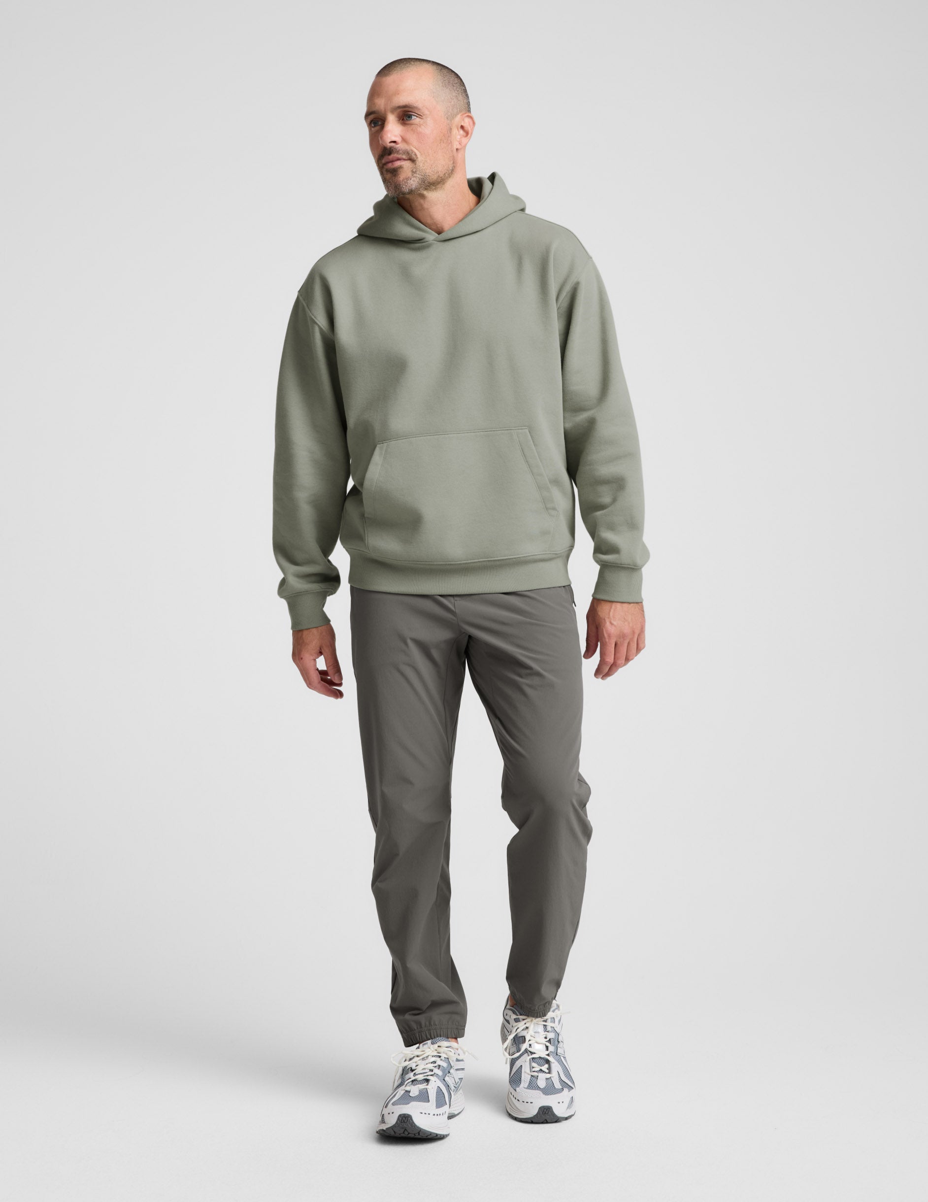 Man wearing a green hoodie and gray pants on a light gray background.