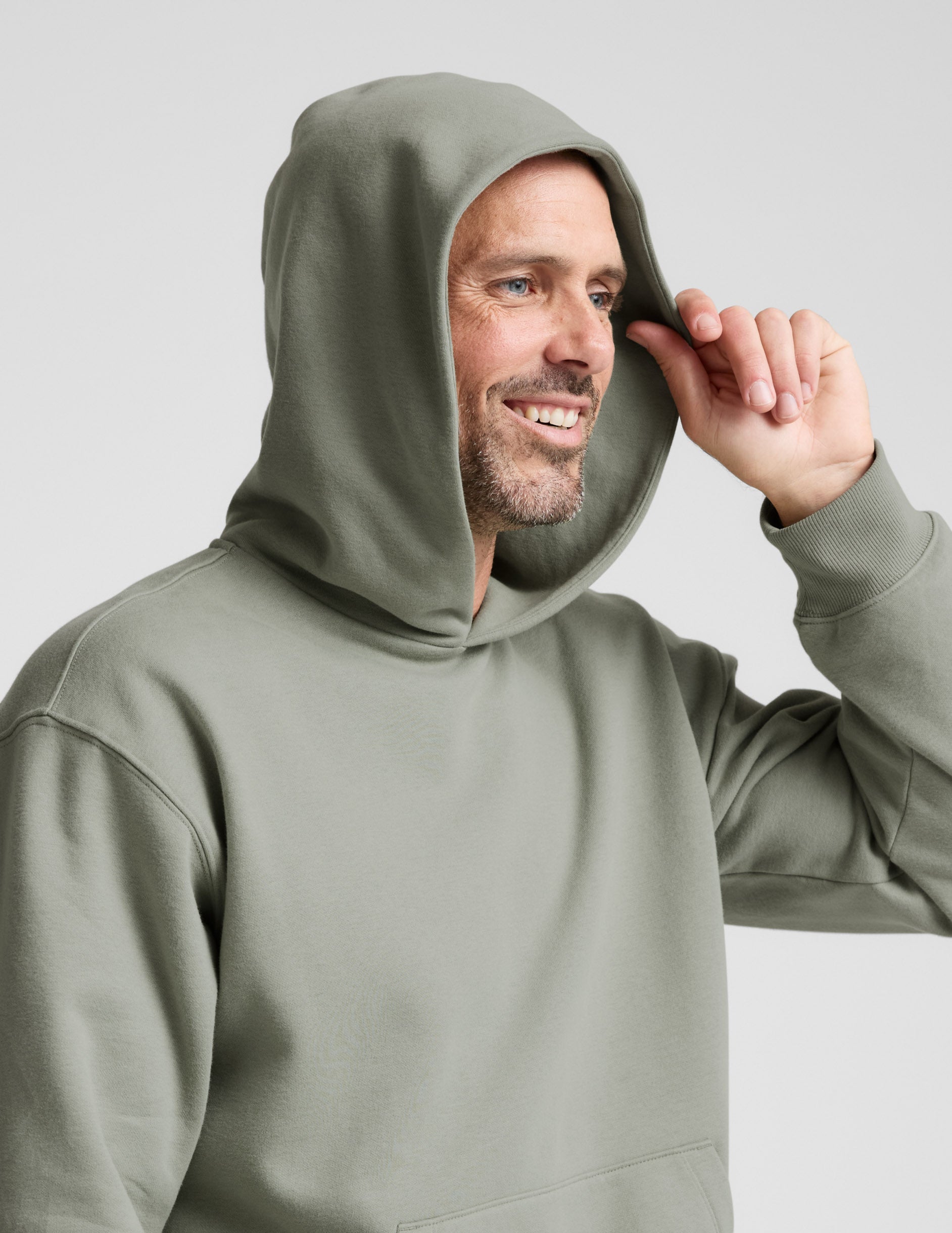 Man wearing a green hoodie and gray pants on a light gray background.