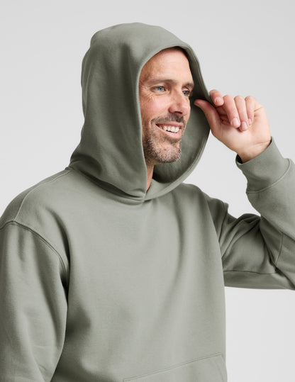 Man wearing a green hoodie and gray pants on a light gray background.