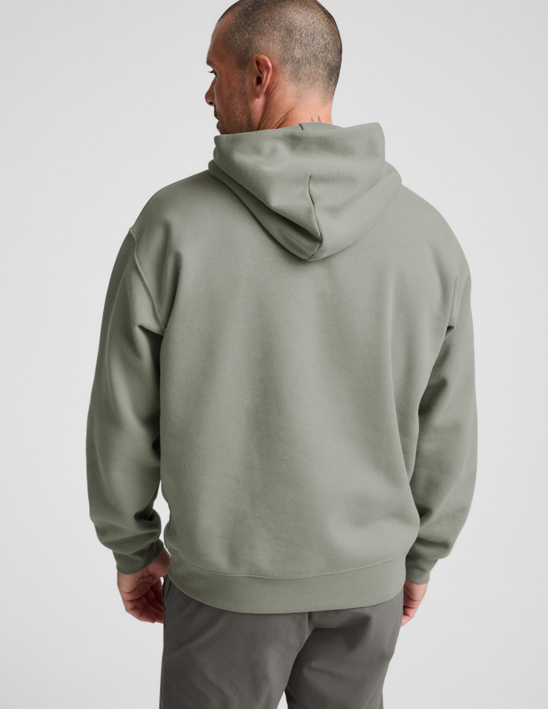 Man wearing a green hoodie and gray pants on a light gray background.