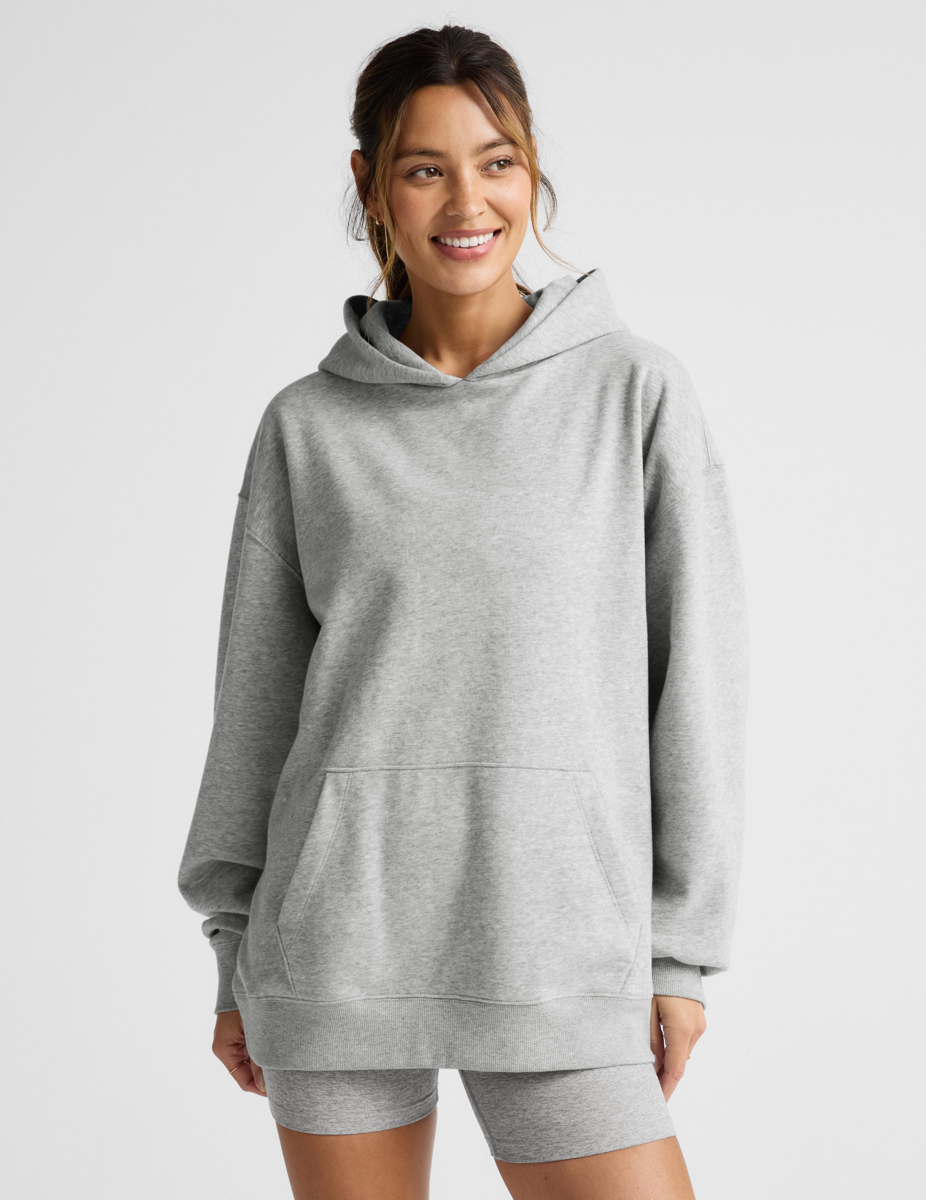 Woman wearing a gray hoodie and shorts set on a light gray background.