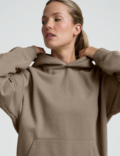 woman wearing a beige hoodie and black leggings on a plain background.