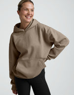 woman wearing a beige hoodie and black leggings on a plain background.
