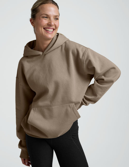 woman wearing a beige hoodie and black leggings on a plain background.
