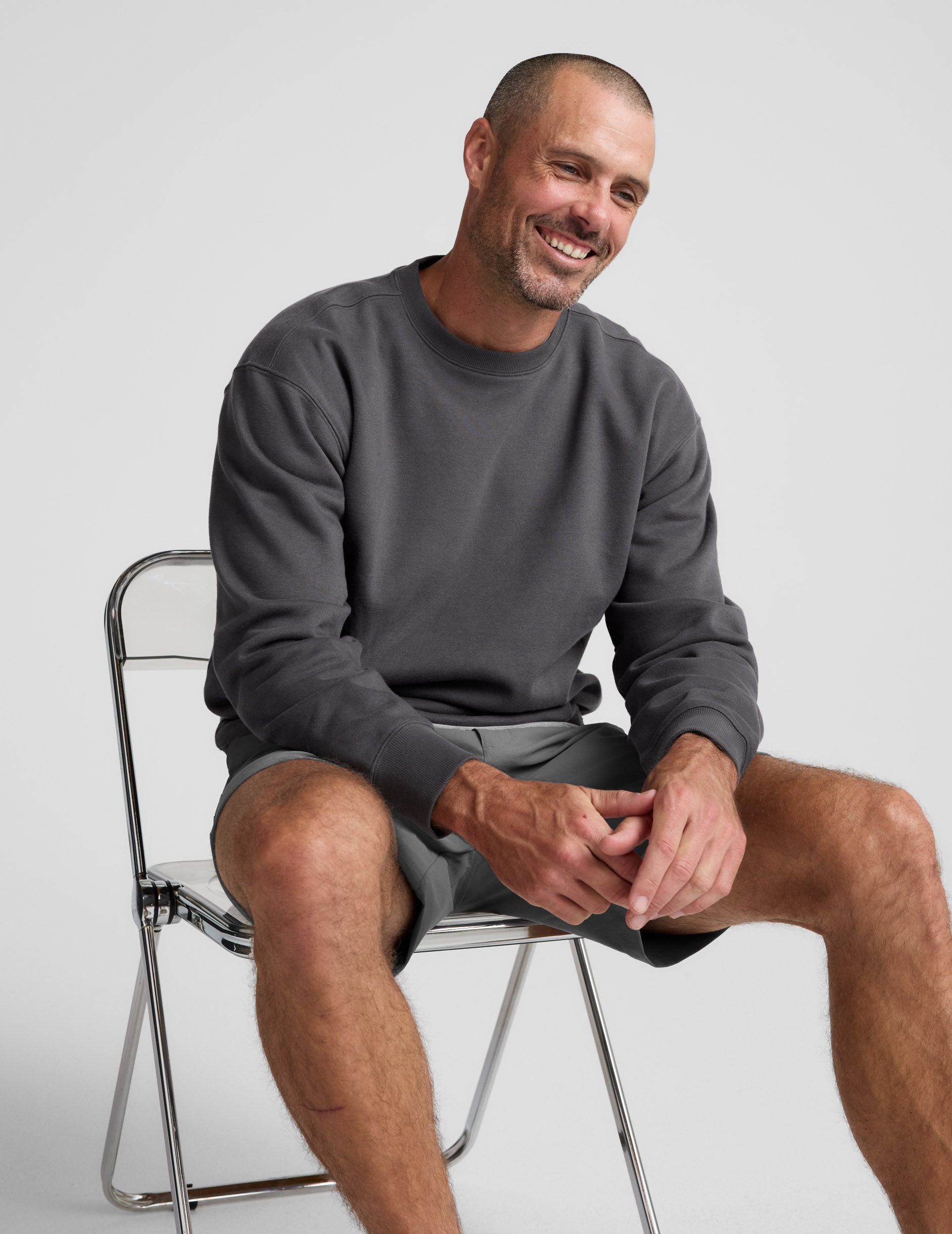 Man wearing a dark gray crewneck sweatshirt and pants on a light background.
