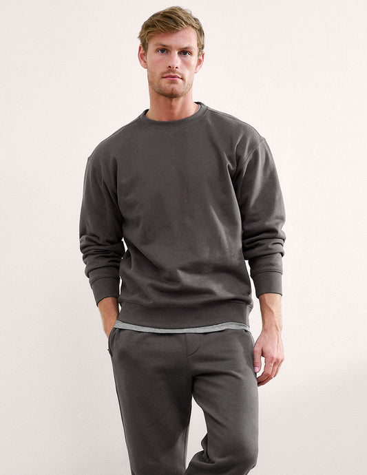 Man wearing a dark gray crewneck sweatshirt and pants on a light background.