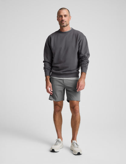 Man wearing a dark gray crewneck sweatshirt and pants on a light background.