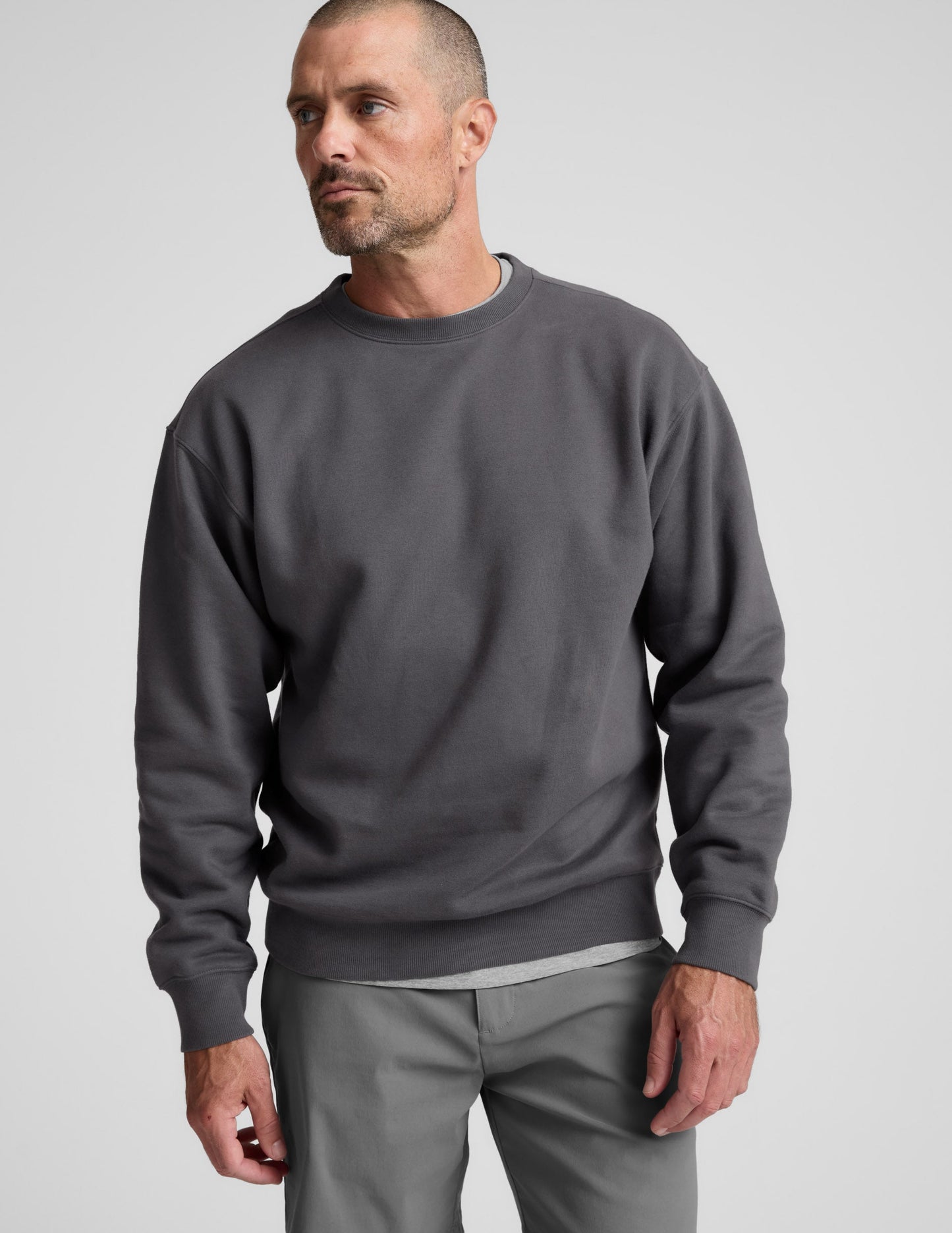 Man wearing a dark gray crewneck sweatshirt and pants on a light background.