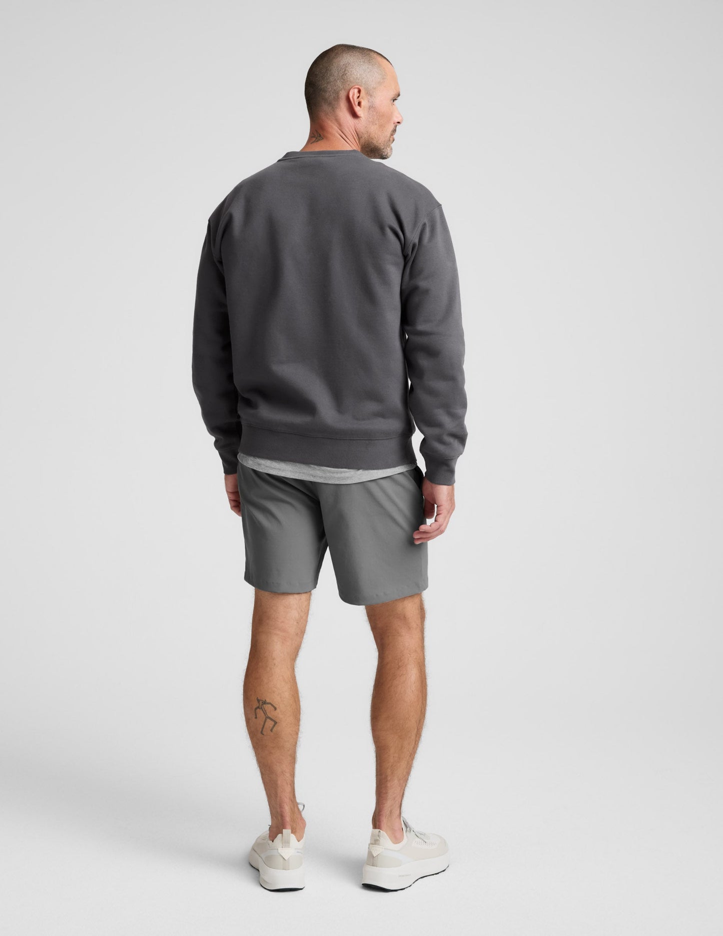 Man wearing a dark gray crewneck sweatshirt and pants on a light background.