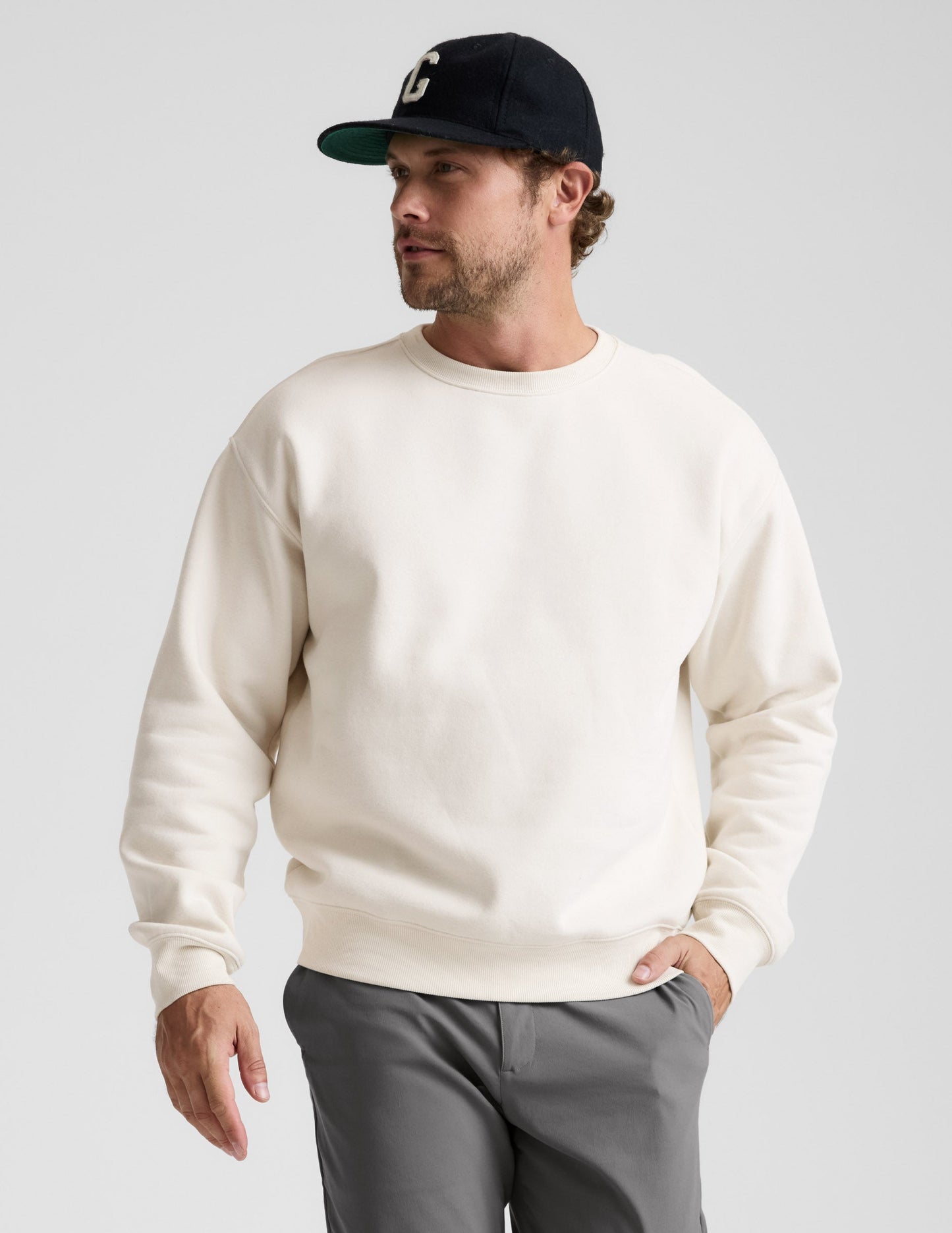 Man wearing a white sweatshirt and gray pants against a plain background.