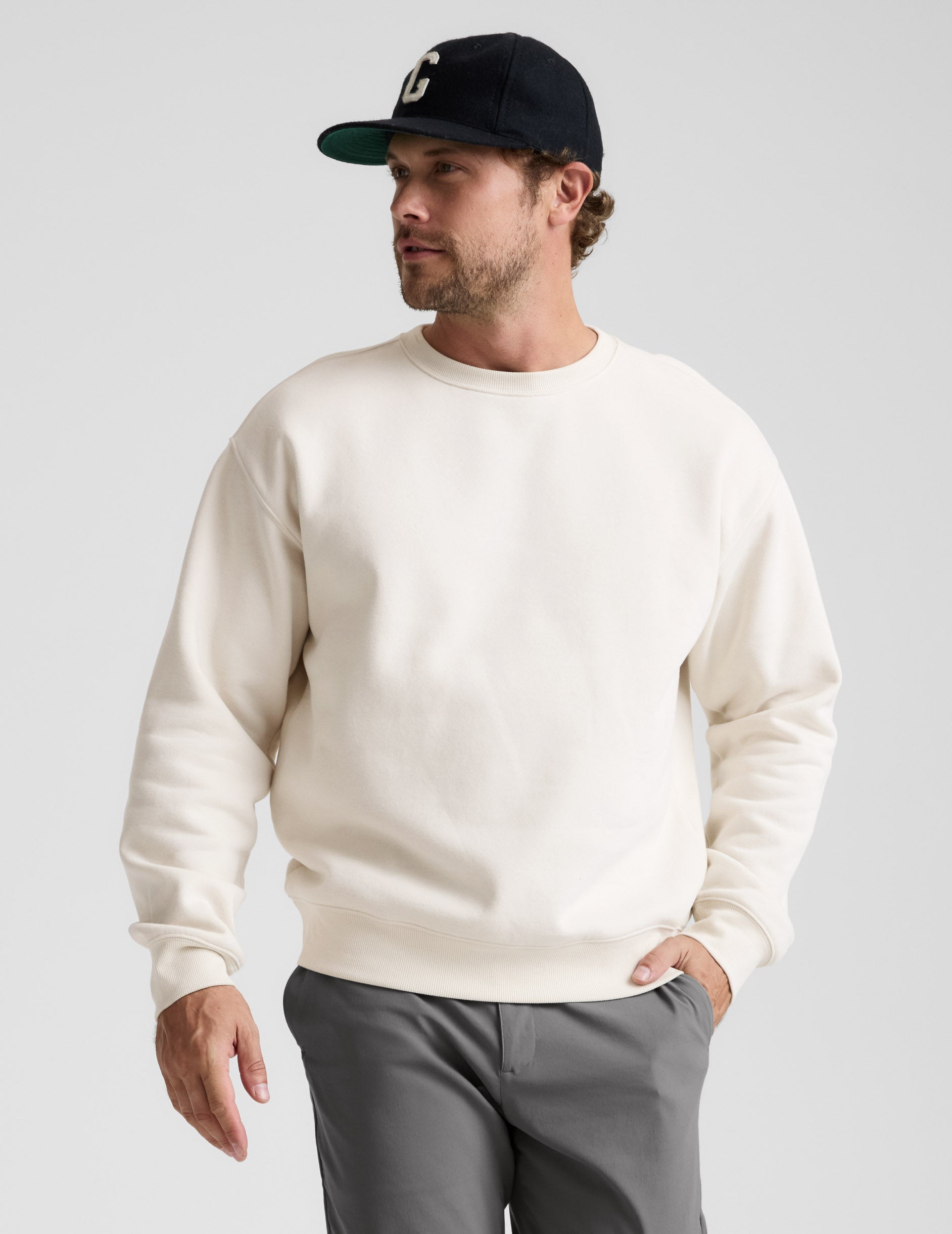 Man wearing a white sweatshirt and gray pants against a plain background.