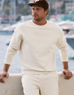 Man wearing a cream colored sweater and cap by a waterfront.