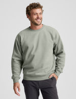 Man wearing a green crewneck sweatshirt and dark pants on a light gray background.