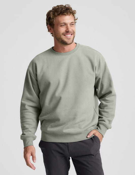 Man wearing a green crewneck sweatshirt and dark pants on a light gray background.