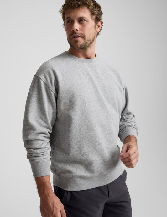 Man wearing a gray sweater and black pants against a plain background.