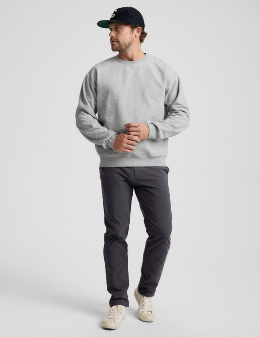Man wearing a gray sweater and black pants against a plain background.